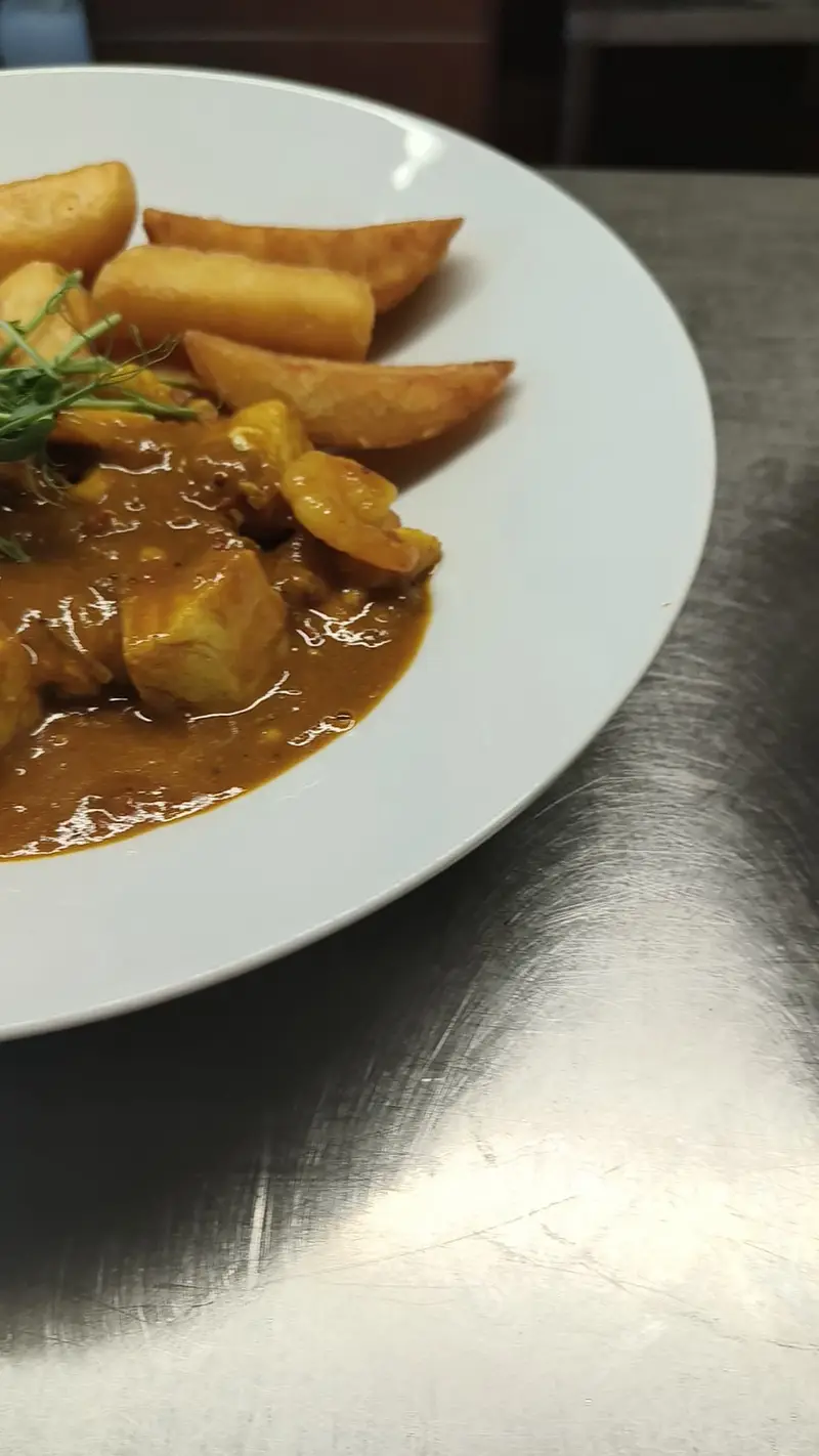 Plate of curry with potato wedges on a table.